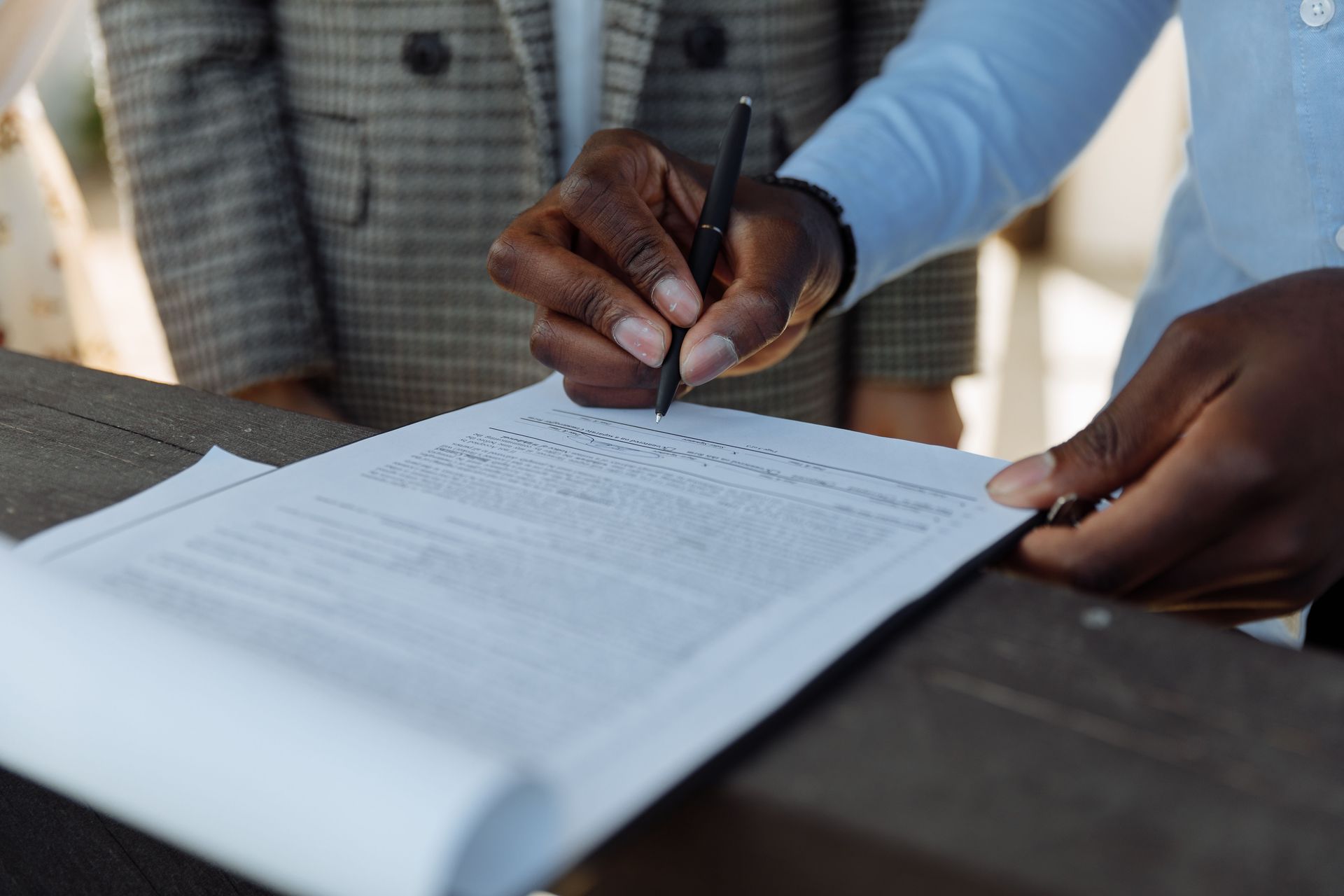Close-up of business professionals signing a document with a pen indoors.